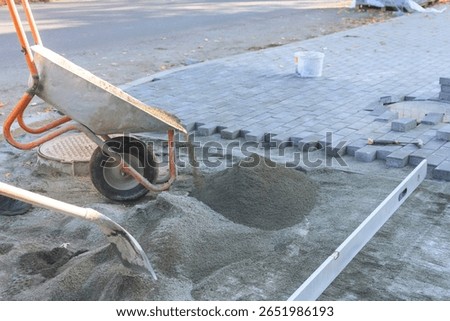Workers are preparing to install pavers on street using wheelbarrow for sand leveling tools for accuracy.