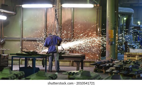 Workers In Protective Equipment In A Foundry Work On A Casting With A Grinding Machine At The Workplace