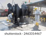 Workers in protective suits and yellow boots clean oily ship blocks at an indian ship recycling yard. This image highlights the meticulous process and safety measures in industrial environments.