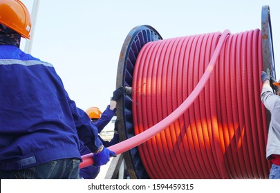 Workers Pulling High Voltage Cable Line Or Large Electric Cable From Big Steel Cable Drum In Chemical Plants, Power Plants, Oil & Gas Industry Or Onshore.