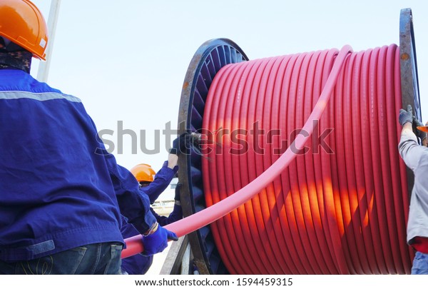 Workers pulling high voltage cable\
line or large electric cable from big steel cable drum in chemical\
plants, power plants, oil & gas industry or\
onshore.