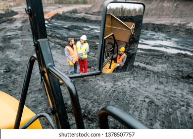 Workers in quarry seen in the mirror of a heavy-duty truck standing in the mud