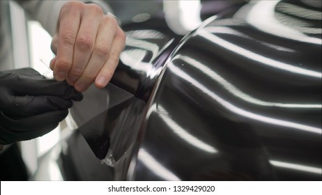 Workers Remove The Protective Film From The Machine.Deteyling Car. Sticker Protective Film On The Bumper Of The Car.