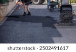 Workers repaving a residential driveway with fresh asphalt.