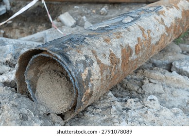 Workers are replacing a damaged sewer pipe in a construction area. The old pipe shows signs of wear and has dirt around it. Tools and materials are visible on site.