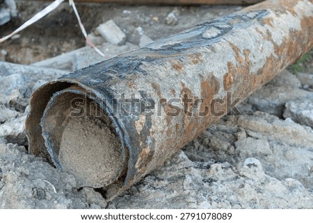 Workers are replacing a damaged sewer pipe in a construction area. The old pipe shows signs of wear and has dirt around it. Tools and materials are visible on site.