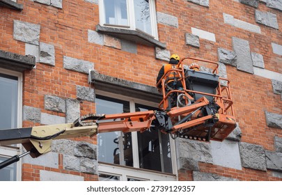Workers restoring building facade using lift equipment, commercial renovation industry.