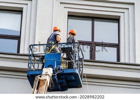 Workers are restoring the facade of the building while standing on a special platform. Home wall repair with the help of a lifting tower. Unrecognizable people