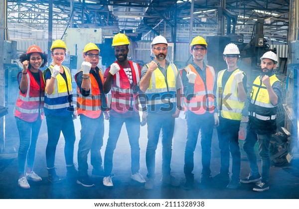 Workers and workers are standing in\
the factory. Group Staff Standing In Engineering\
Factory.