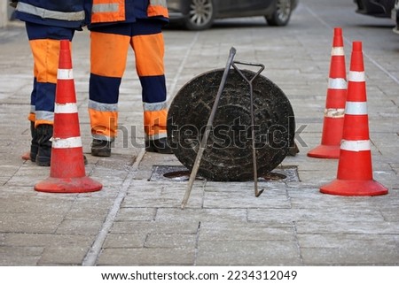 Workers standing over the open sewer hatch on winter street on cars background. Concept of repair of sewage, underground utilities, cable laying under the road