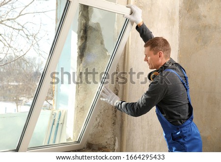Workers in uniform installing plastic window indoors