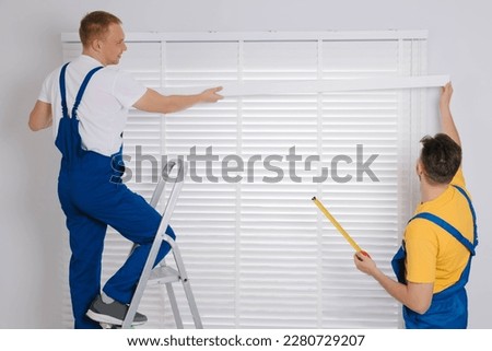 Workers in uniforms installing horizontal window blinds indoors