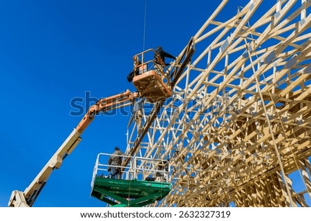 Workers use machinery to construct trusses wooden framework under bright blue sky in work area