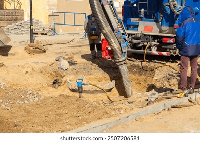 Workers use a suction excavator based on a truck to sample soil in a well for communications during restoration work on a street.