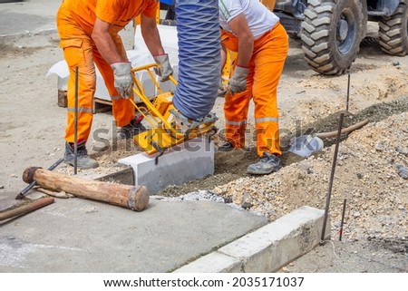 Workers using machine to align and set the concrete curbs. Concrete kerb installation at sidewalk edging.
