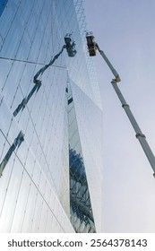 Workers using a mechanical lift to clean or maintain the reflective glass facade of a modern building