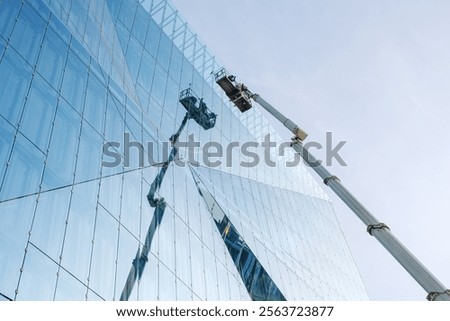 Workers using a mechanical lift to clean or maintain the reflective glass facade of a modern building