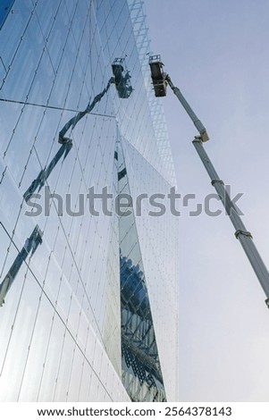 Workers using a mechanical lift to clean or maintain the reflective glass facade of a modern building