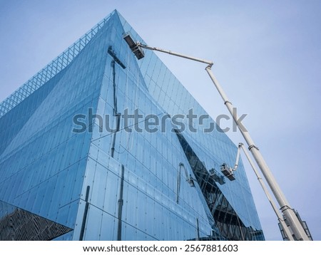 Workers using a mechanical lift to clean or maintain the reflective glass facade of a modern building