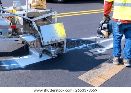 Workers are using road marking machine to apply white paint on new asphalt surface in city setting.