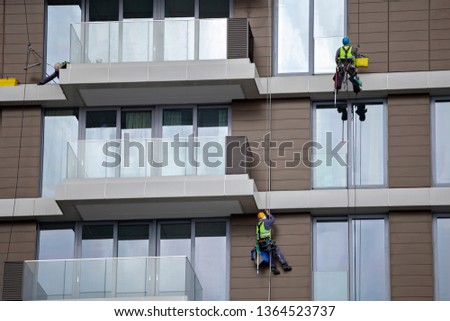 Workers using rope to clean a high apartment building, steeplejack works. Mountain climber washes windows.