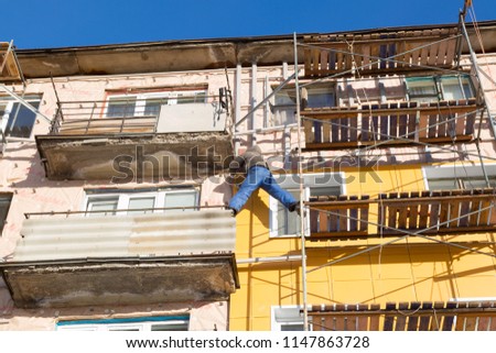 Workers warm and repair the facade of the building. The old house is compacted with mineral wool and the exterior of the building is lined. Work at height without insurance