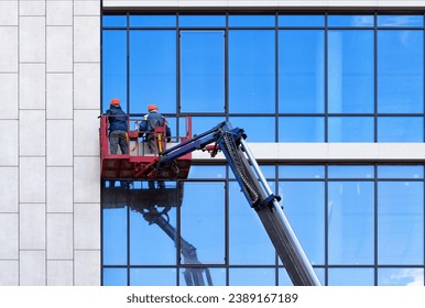 Workers wash glass windows of an office building in a crane bucket.