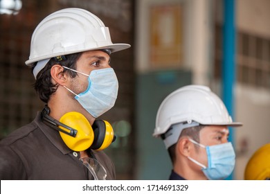 Workers wear protective face masks for safety in machine industrial factory. - Shutterstock ID 1714691329
