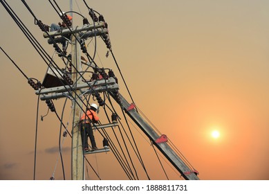 Workers Wearing Safety Harness Full Or Electrician Working On Checking And Inspection Equip On The Electric Pole On Sunset Background