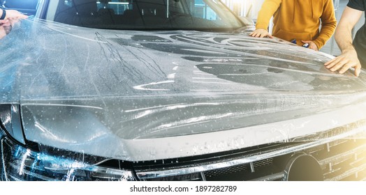 Workers Wrap Wet Paint Protection Film Or Anti-gravel Protection Coating On New Car Hood. Car Detailing