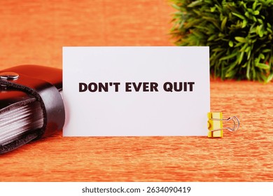 Workforce Reduction, Downsizing, Reorganization, Restructuring concept. Text DO NOT EVER QUIT written on a card on a bright orange table next to a black notebook and a small green plant