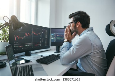 Working All Day...Side View Of Tired Young Businessman Or Trader Working With Charts On Computers At His Modern Office.