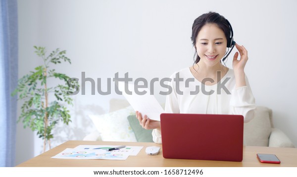 Working asian woman in the living room.\
Telemeeting. Video conference. Remote\
work.