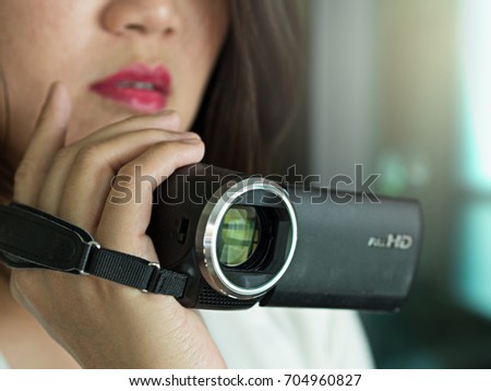 Working Asian woman recording or taking a media video using video recorder, camcorder or video camera, close up face and hand