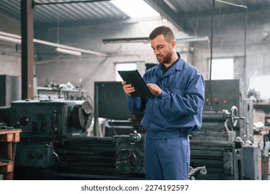 Working by using digital tablet. Man at the factory that is in blue uniform is indoors. - Powered by Shutterstock