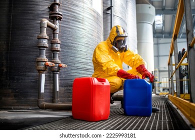 Trabajando en la fábrica de producción de productos químicos. Trabajador profesional con traje de neblina protector y máscara de gas que manipula sustancias químicas peligrosas junto a grandes depósitos de metal.