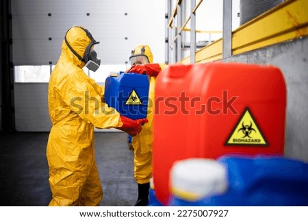 Working in chemicals production factory. Professional workers in protection suit and gas masks lifting plastic canisters with hazardous and toxic materials.