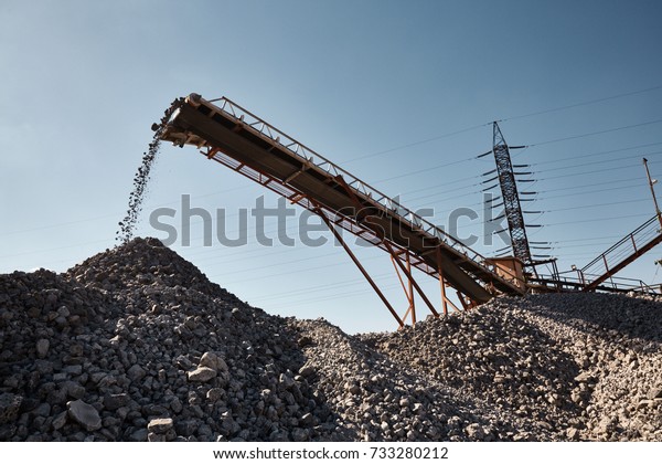 Working conveyor belt on slag transportation\
and loading. Heavy industrial metallurgical landscape with power\
lines on background