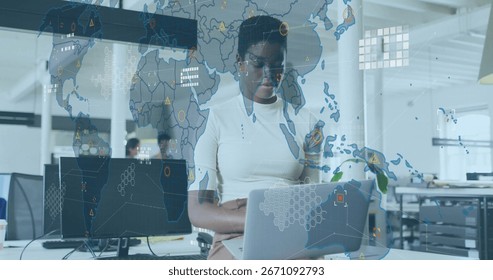 Working data analyst typing on silver laptop in open-plan office, with digital world map overlay. Collaboration, technology, workspace, innovation, digital, modern, teamwork