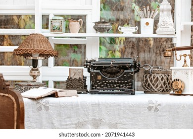 Working Desk With Vintage Old Fashioned Typewriter Machine Underwood, Antique Lamp, Retro Phone, Books Next To Window In Light Shabby Chic Country Cottage Interior Room
