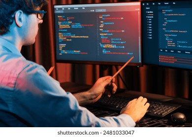 Working IT developer pointing with pencil on online software development coding database application on pc screens, creating program for firmware on website at neon light modern office home. Gusher.