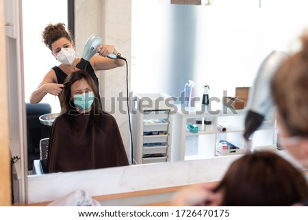 Working during covid-19 or coronavirus concept. A professional hairdresser cutting the hair to a client, reflected in the mirror with copy space.