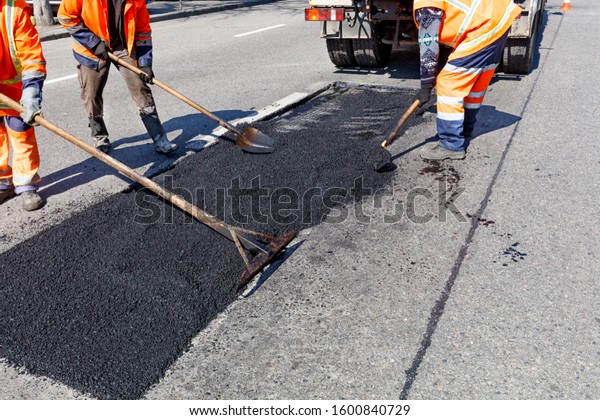 A working group of road workers accurately levels\
fresh asphalt on a part of the road for repair in road\
construction, image with copy\
space.