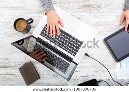 A working womanâ??s hand at a table with laptop,tablet and phone.