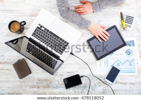 A working womanÃ¢??s hand at a table with laptop,tablet and phone.