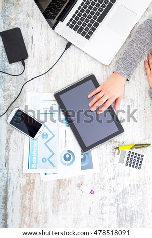 A working womanÃ¢??s hand at a table with laptop,tablet and phone.