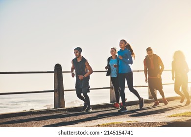 Working Hard To Conquer That Inner Couch Potato. Shot Of A Fitness Group Out Running On The Promenade.