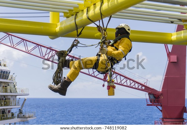 Working at height. Working overboard. A\
commercial abseiler with fall arrestor device hanging on bridge\
pipeline structure at oil and gas\
platform.