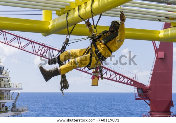 Working at height.\
Working overboard. A commercial abseiler with fall arrestor device\
hanging on bridge pipeline structure at oil and gas platform to\
perform painting works.