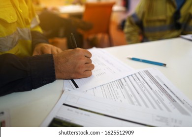 Working at heights permit book placing on the table, defocused construction site supervisor reviewing job hazard analysis risk safety assessment prior approval and sign off work on open field 